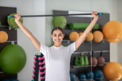 Body,Workout.,Smiling,Dark haired,Female,Stretching,Her,Shoulders,With,Stick,